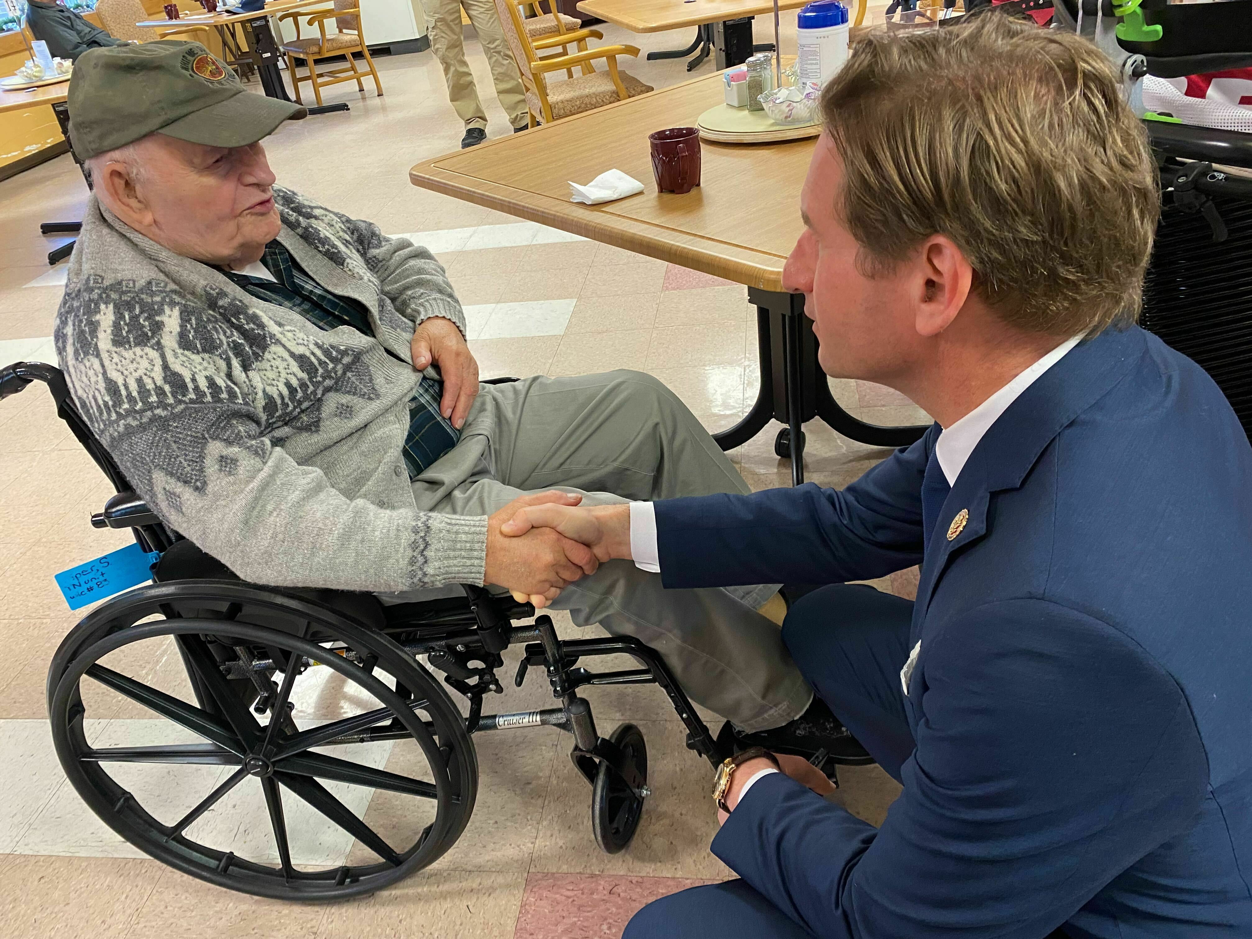 caption: Stanley Piper talks with Rep. Dean Phillips, D-Minn., at the New Hampshire Veterans Home in Tilton, N.H. on Dec. 8, 2023.