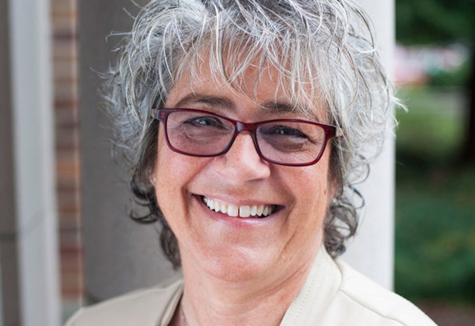 A woman with short gray hair and dark red glasses smiles at the camera. 