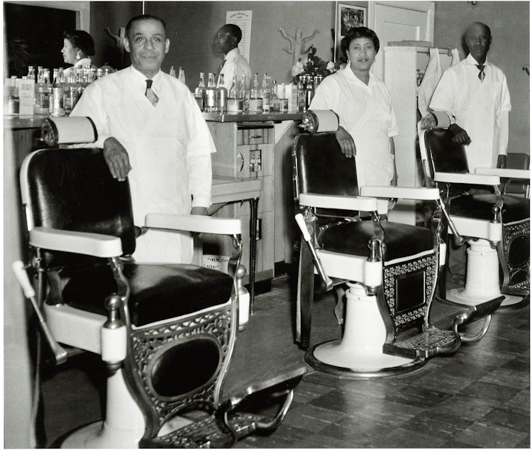 caption: Bertha M Johnson, owner of Bertha's Barber Shop on 23rd Avenue, center, with two male barbers. Many of the cosmetologists in Seattle's Central District were trained at Marie Edwards School of Beauty on Jackson Street, which was the only African American-owned beauty school in the Pacific Northwest. (To help us ID the two male barbers, note the photo number. This is #5.)