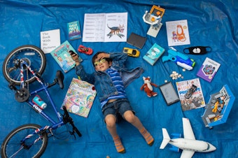 caption: Elizabeth Dalziel's son Joe, 7, lays next to his favorite objects, toys and books as part of a homeschooling assignment — to create a time capsule — from his school in Berkhamsted, England.