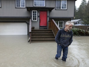 caption: Bernie Crouse wades through water outside his home after the nearby South Fork Stillaguamish River crested early in the morning flooding several houses in this neighborhood, Dec. 5, 2023, in the Arlington area of Seattle, Washington.