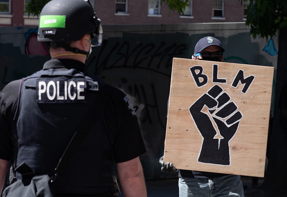 caption: A police officer stands in front of a Black Lives Matter sign during a protest in front of Seattle City Hall on August 9, 2020.