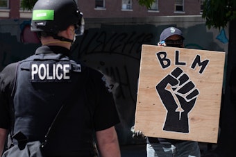 caption: A police officer stands in front of a Black Lives Matter sign during a protest in front of Seattle City Hall on August 9, 2020.