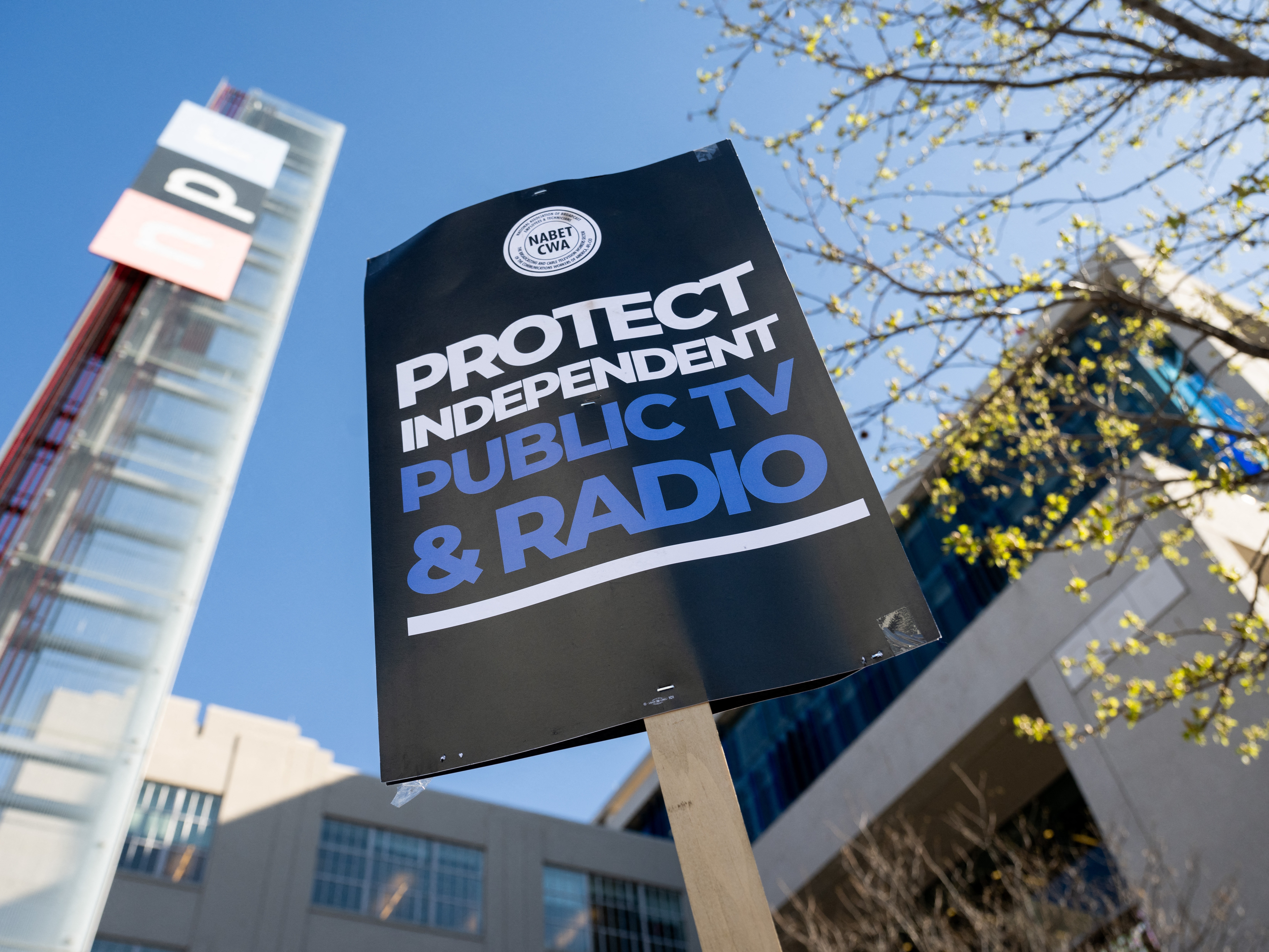 caption: People participate in a rally to call on Congress to protect funding for US public broadcasters, Public Broadcasting Service (PBS) and National Public Radio (NPR), outside the NPR headquarters in Washington, DC, on March 26, 2025.
