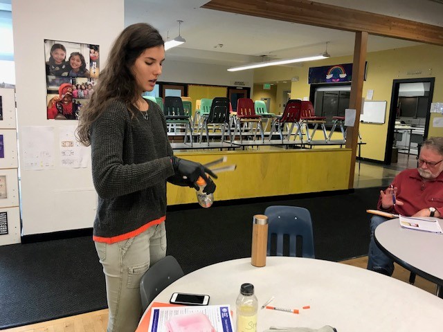 caption: Seattle Public Utilities Alison Steinbacher, demonstrates how to pick up used needles safely. 