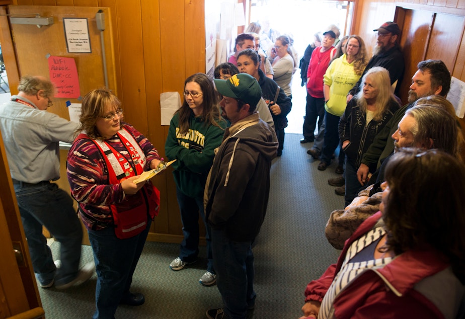 caption: In the entryway to the Darrington Community Center, Red Cross Volunteer Christine Dahl works through the list of area residents seeking gas cards to help with the cost of traveling the two and a half hour detour created by the devastating mudslide.
