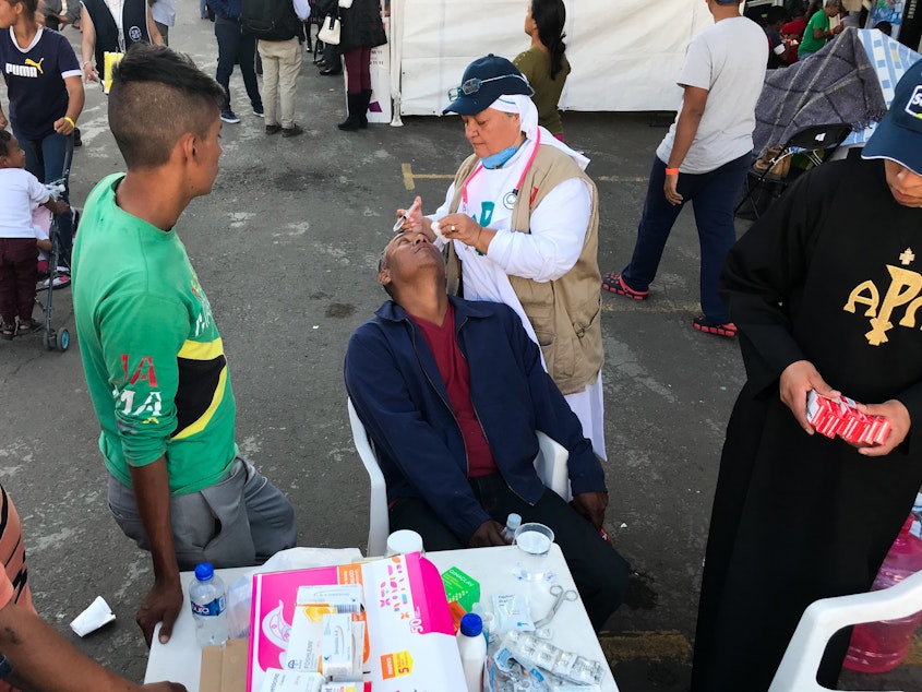 caption: Sister Bertha Lopez Chaves applies anti-inflammatory eyedrops to a migrant at a stadium in Mexico City where the caravan is resting. Her order is one of roughly 50 groups giving aid to the migrants in the Mexican capital. "We're just trying to deal with their basic needs so they can continue on," she says.