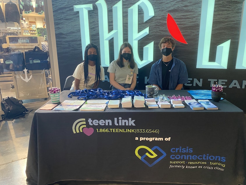caption: (From left) Chloe Burton, Isobel Wright and Zane Reed volunteer at the Teen Link booth during a recent event at Climate Pledge Arena. Burton and Reed are teen volunteers. 