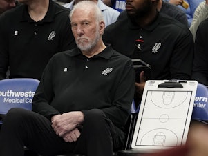 caption: San Antonio Spurs beach coach Gregg Popovich sits on the bench during the first quarter of an NBA basketball game against the Dallas Mavericks in Dallas, Sunday, April 9, 2023.