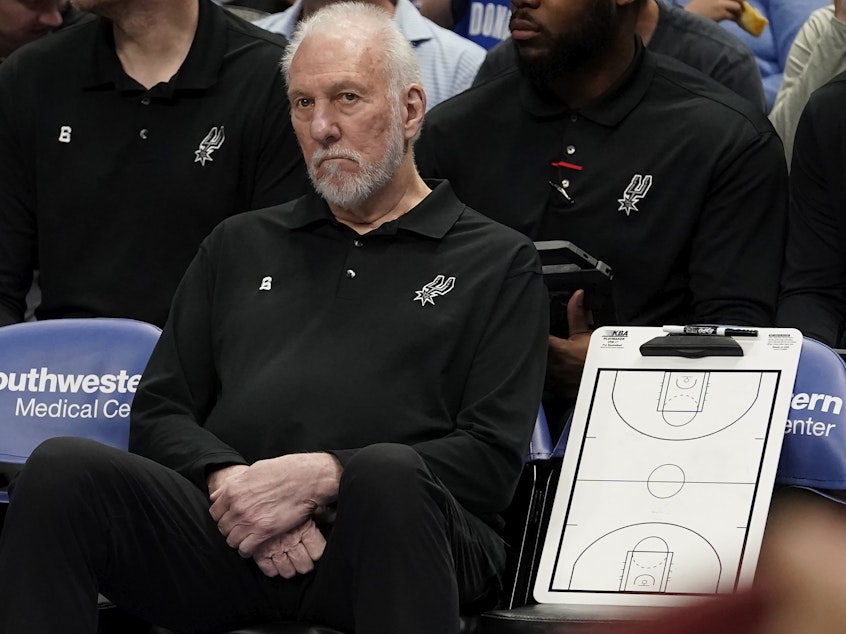 caption: San Antonio Spurs beach coach Gregg Popovich sits on the bench during the first quarter of an NBA basketball game against the Dallas Mavericks in Dallas, Sunday, April 9, 2023.