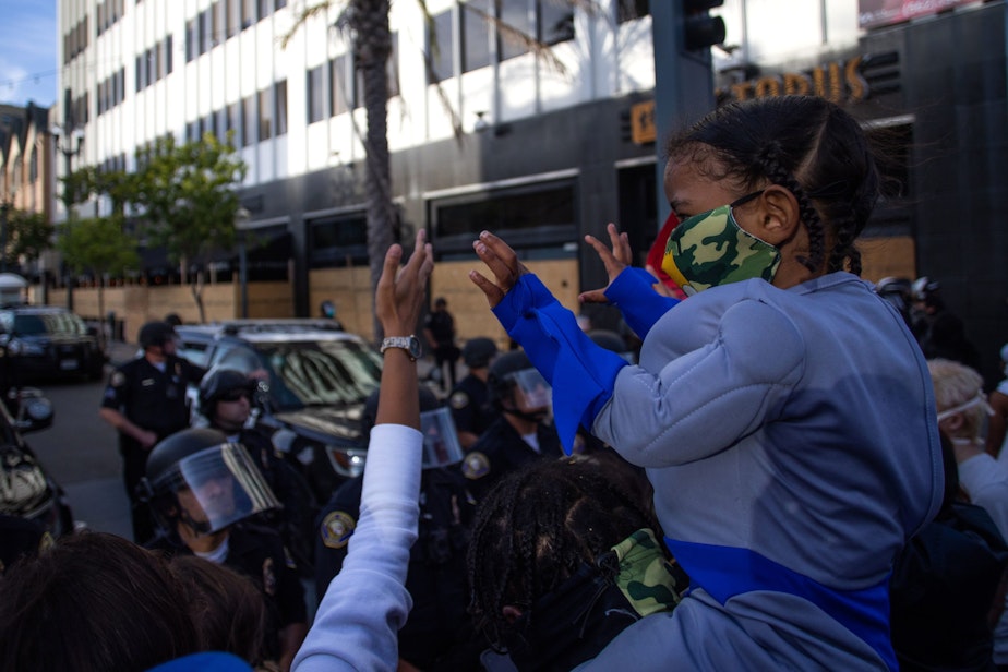 caption: A child holds up his hands in front of a row of police officers in downtown Long Beach on May 31, 2020 during a protest against the death of George Floyd, an unarmed black man who died while being arrested and pinned to the ground by the knee of a Minneapolis police officer. (APU GOMES/AFP via Getty Images)