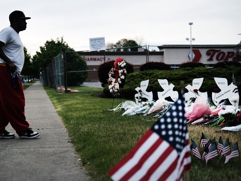 caption: A person stands at a memorial for the victims of the May 2022 shooting at a Tops supermarket in Buffalo, N.Y.