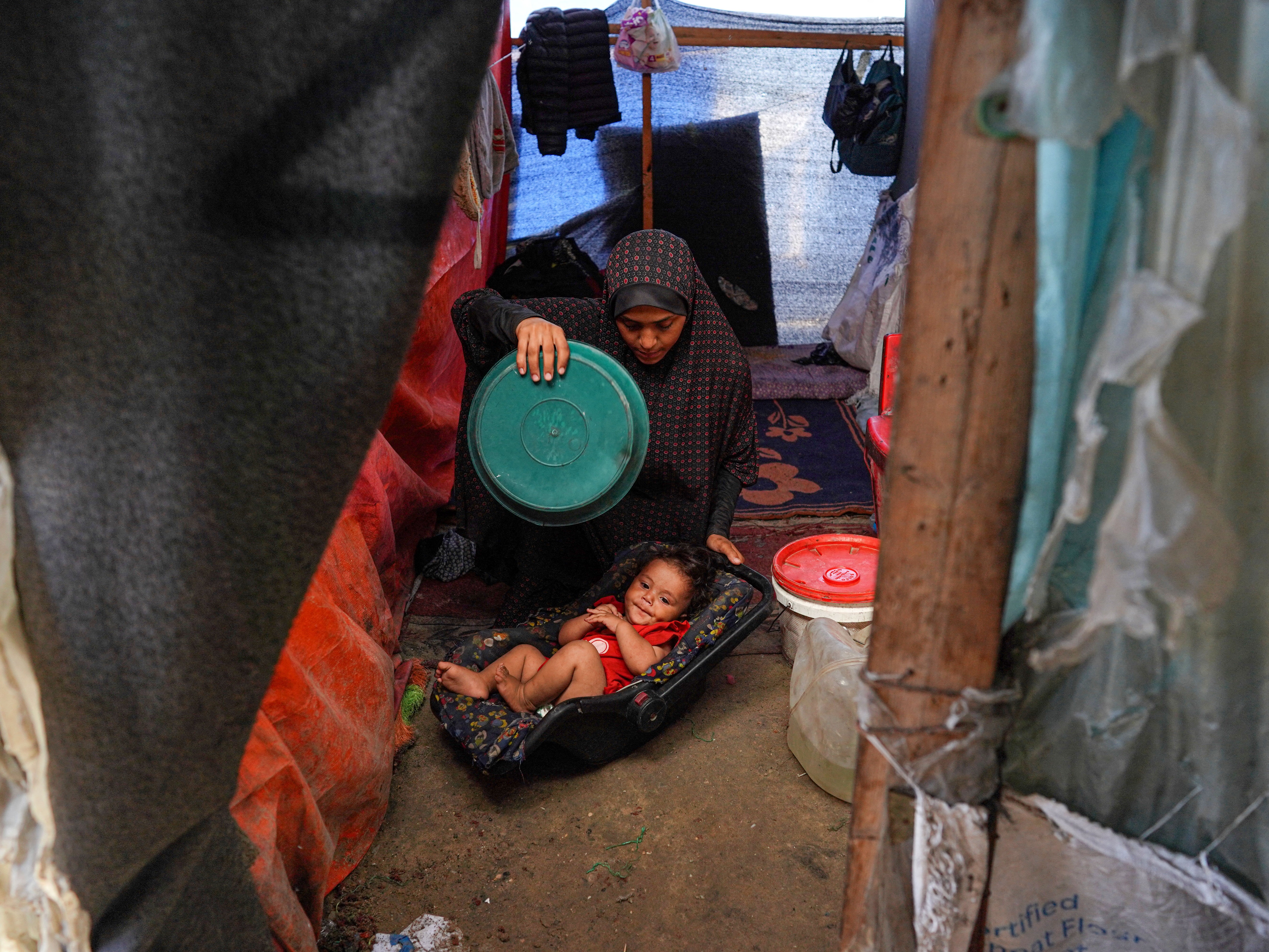 caption: A Palestinian woman uses a plastic plate to fan a baby during a heatwave in Gaza in 2024.