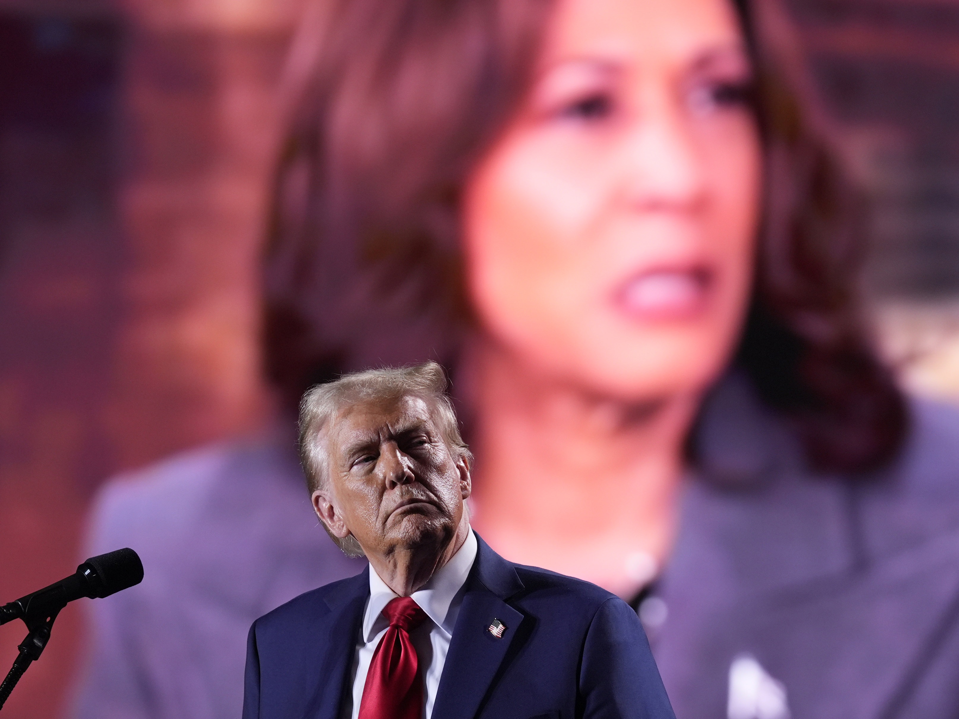 caption: Republican presidential nominee and former President Donald Trump watches as a video featuring Vice President Harris, the Democratic presidential nominee, plays during a campaign event on Oct. 18 in Detroit.