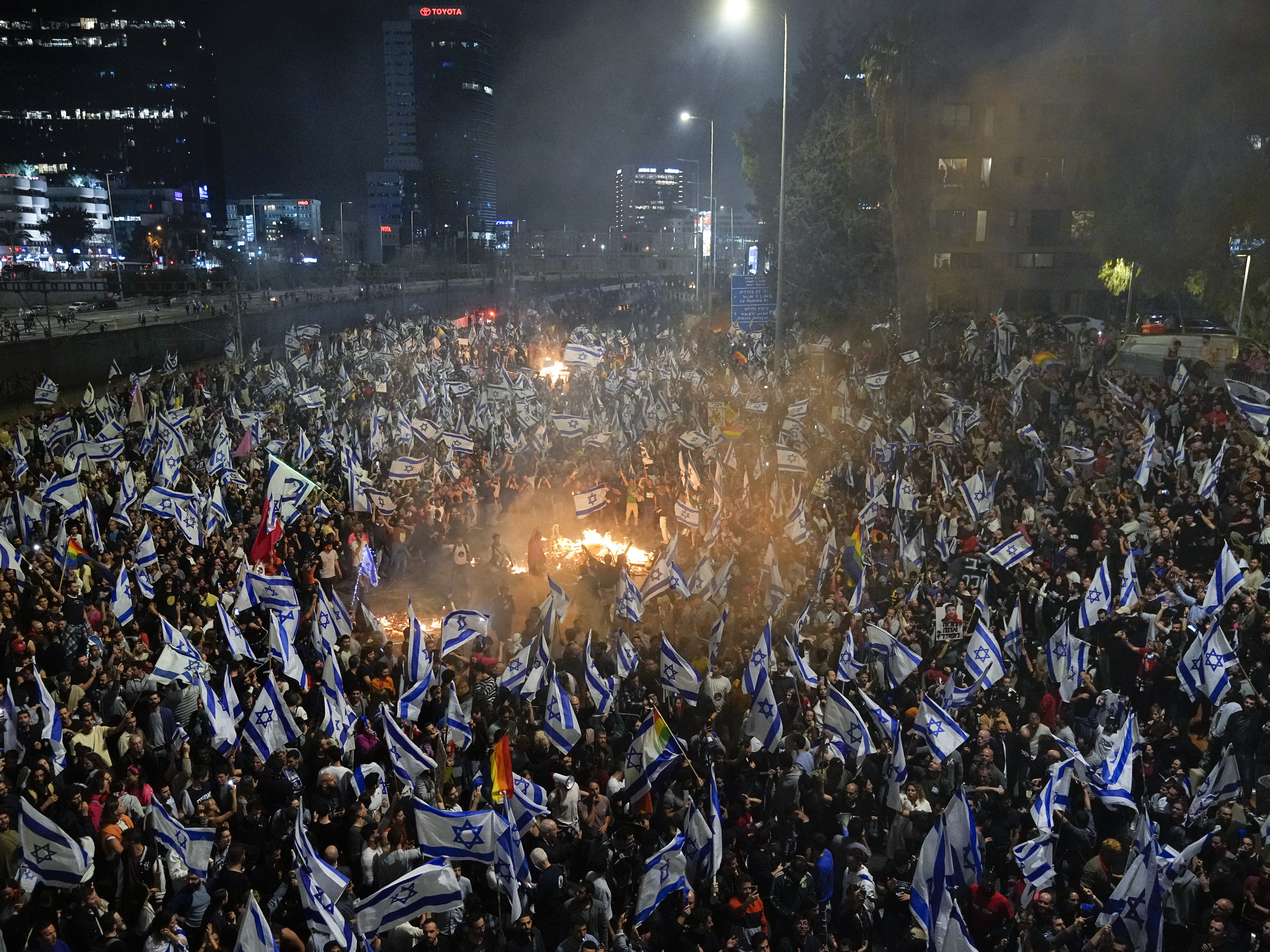 caption: Israelis opposed to Prime Minister Benjamin Netanyahu's judicial overhaul plan set up bonfires and block a highway during a protest moments after the Israeli leader fired his defense minister, in Tel Aviv, Israel, Sunday, March 26, 2023.