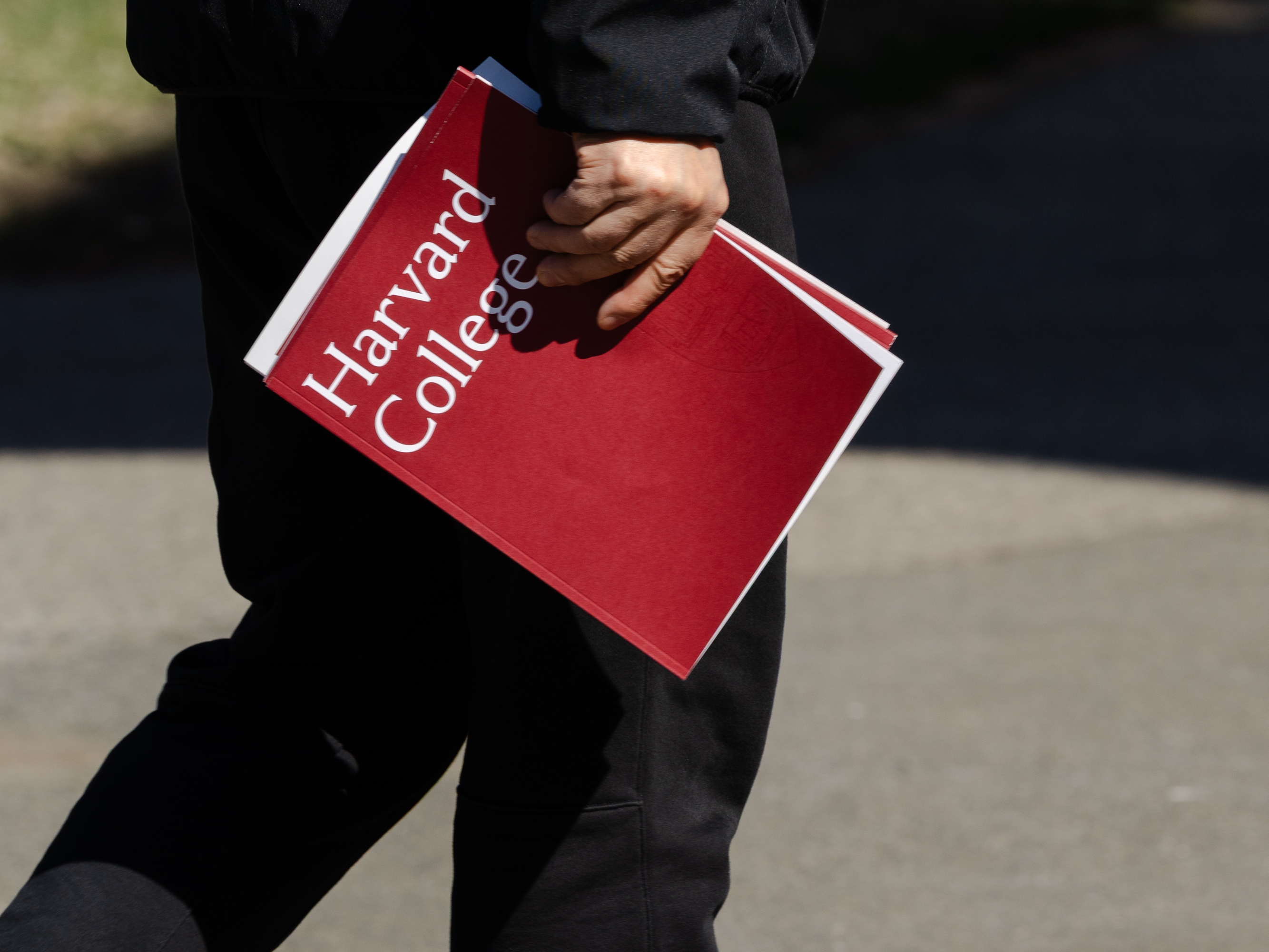 caption: A person holds a Harvard College folder during a tour at Harvard University on April 17 in Cambridge, Mass.