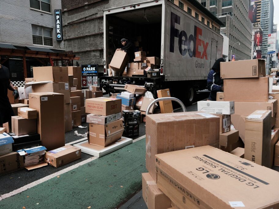 caption: Dozens of packages are lined up along a Manhattan street as a FedEx truck makes deliveries on Dec. 6, 2021, in New York City.