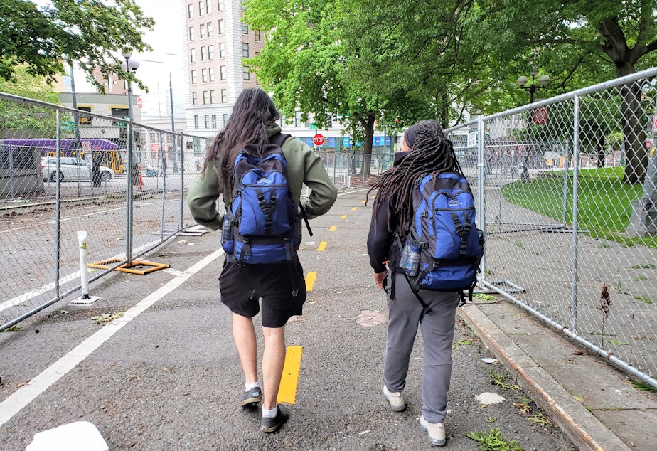 caption: Kirk Rodriguez (left) and Shelby George walk around City Hall Park checking in with people on Wednesday, June 17, 2022.