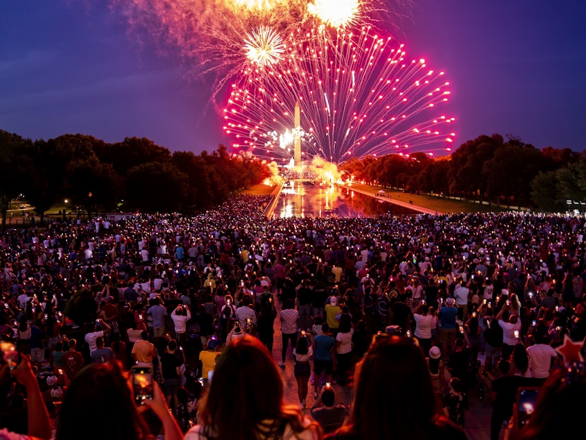 caption: Spectators watch as fireworks erupt over the Washington Monument on July 4, 2022, in Washington, D.C.