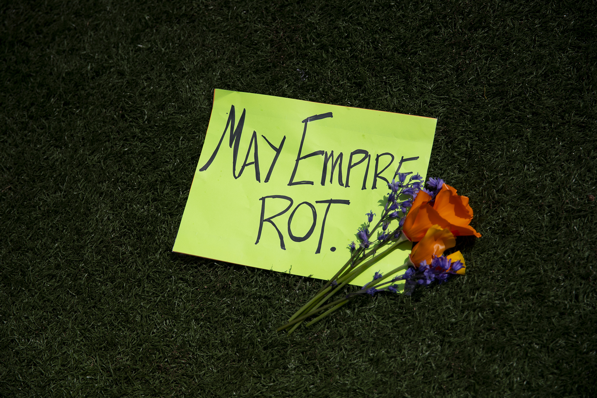 caption: “May Empire Rot” reads a handmade sign with flowers as the annual May Day rally begins on Friday, May 1, 2026, at Cal Anderson Park in Seattle. 