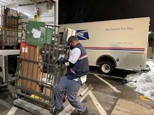 caption: Like many of his colleagues, postal worker Rickey Ramirez is working overtime to keep up with the crush of Christmas deliveries. Many packages are likely to be delivered after Dec. 25.