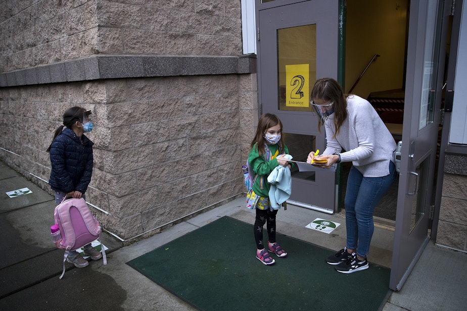 caption: General school assistant Vicki Premo, right, checks in second-grade student Cora on Thursday, January 21, 2021, as second-grade students returned to in-person learning at Somerset Elementary School in Bellevue. 
