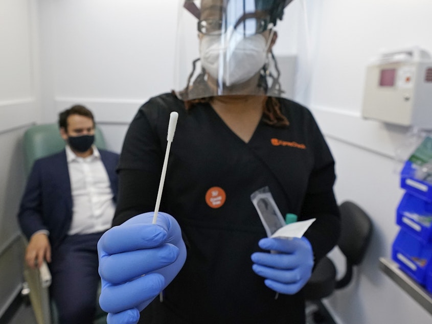 caption: A medical assistant holds a swab after testing a man on Wednesday at the new COVID-19 testing facility at Boston Logan International Airport.