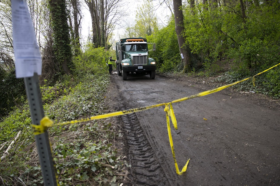 caption: A former encampment in Ravenna is roped off as crews clear out the area with a garbage truck on Wednesday, April 18, 2018, in Seattle. 