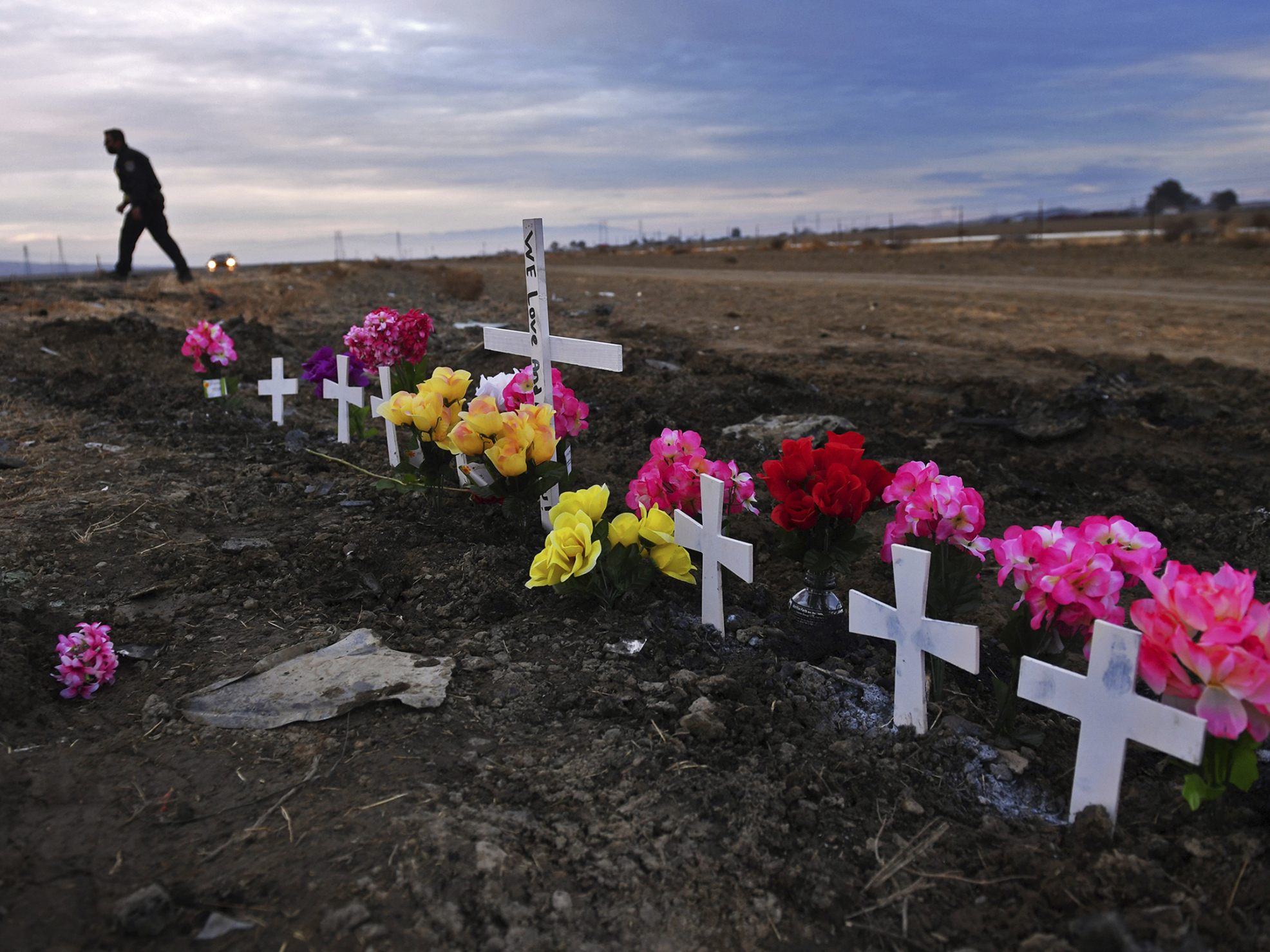 caption: A row of crosses form a memorial along Highway 33 as police officers survey the scene a day after a crash killed nine people south of Coalinga, Calif., on Jan. 2, 2021.