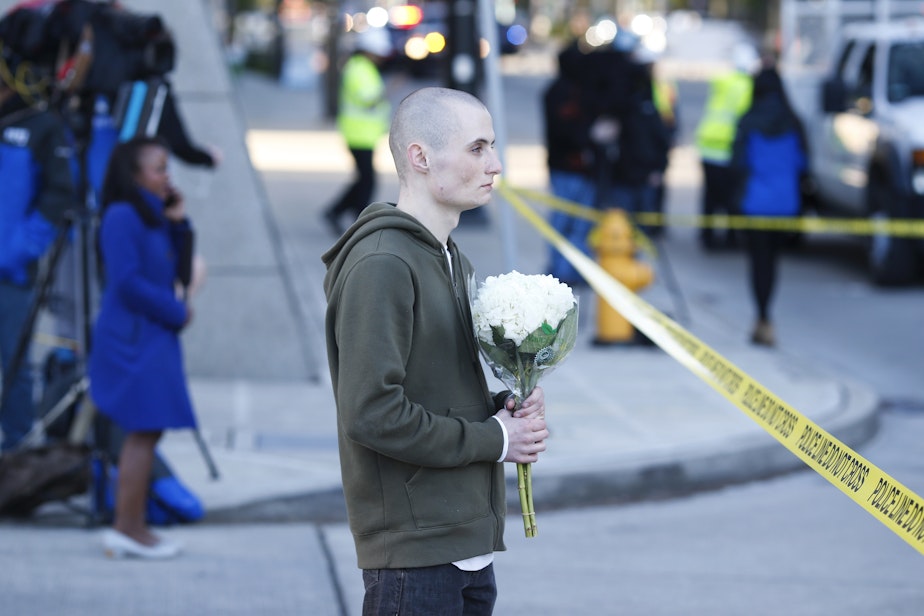 caption: Blake Haner, a Seattle resident, holds flowers for those who died at the scene of a construction crane collapse where several people were killed and several others injured Saturday, April 27, 2019, in the South Lake Union neighborhood of Seattle.
