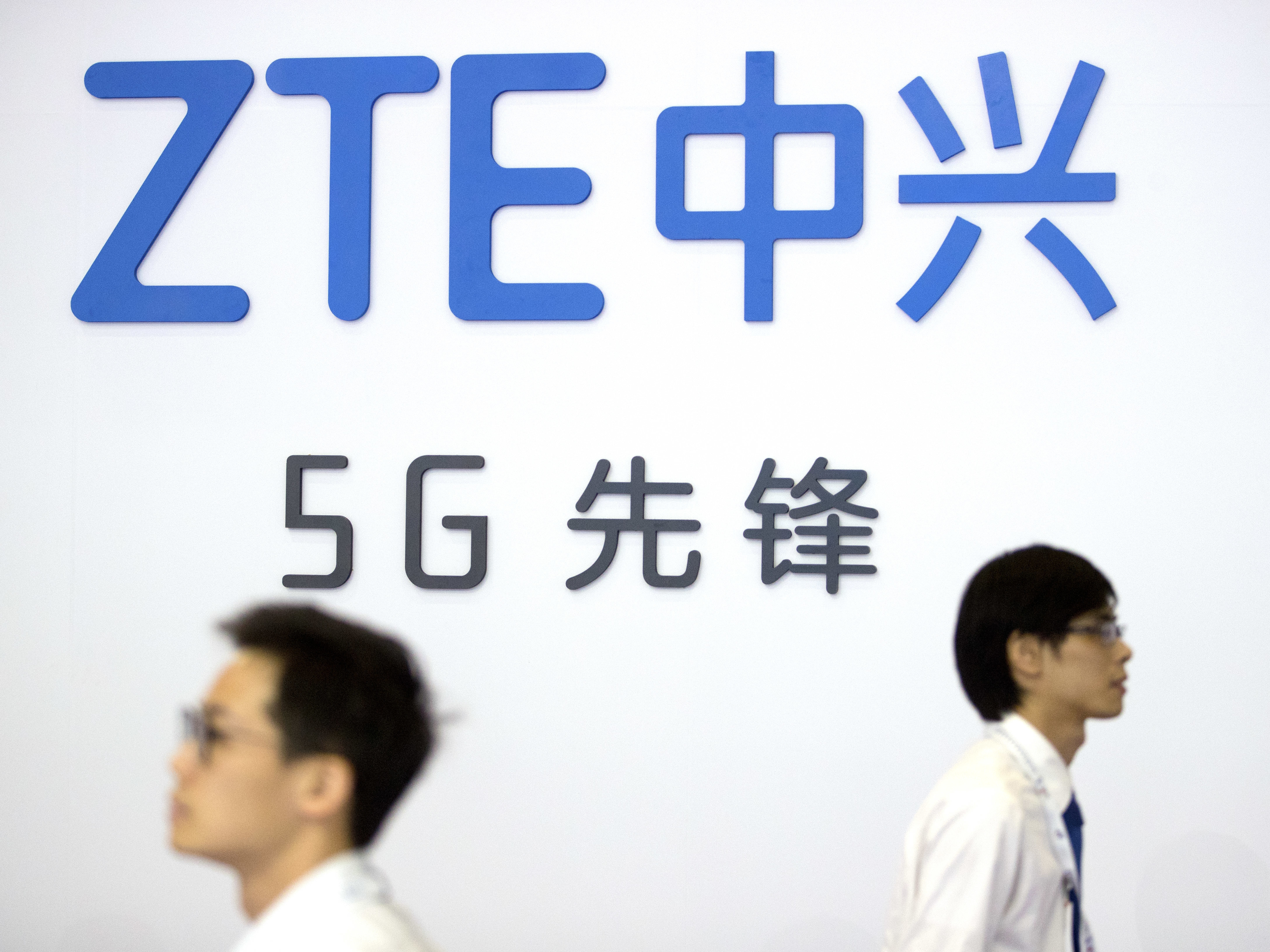 caption: In this Sept. 26, 2018 file photo, visitors walk past a display from Chinese technology firm ZTE at the PT Expo in Beijing.