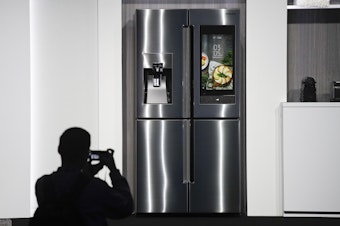 caption: FILE- In this Jan. 8, 2018, file photo, an attendee takes pictures of the new Samsung Family Hub smart refrigerator during a news conference at CES International in Las Vegas. Payment networks and manufacturers are building payment functions into more devices. Samsung’s Family Hub refrigerator lets users order groceries from the Groceries by Mastercard app. 