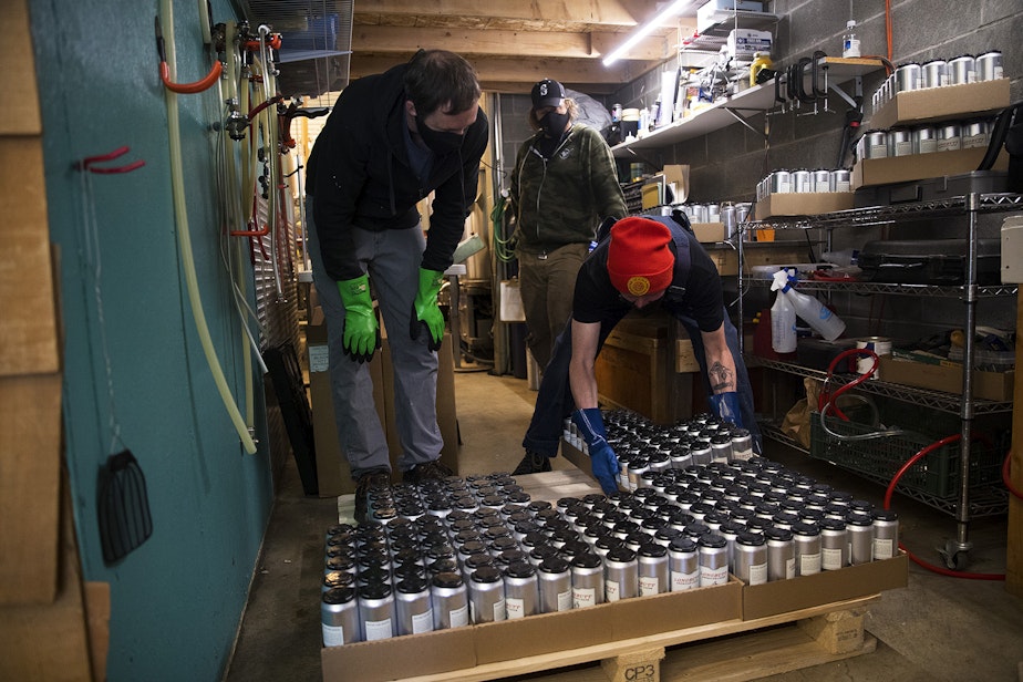 caption: From left, Chris Smith, Scott Jones and John Marti, right, arrange boxes of canned beer from a mobile canning unit onto a pallet on Friday, May 22, 2020, at Lowercase Brewing in Seattle.
