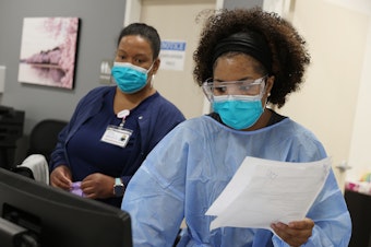 caption: Workers at an urgent care facility in Woodbridge, Va., check health records while testing patients for COVID-19 on April 15, 2020.