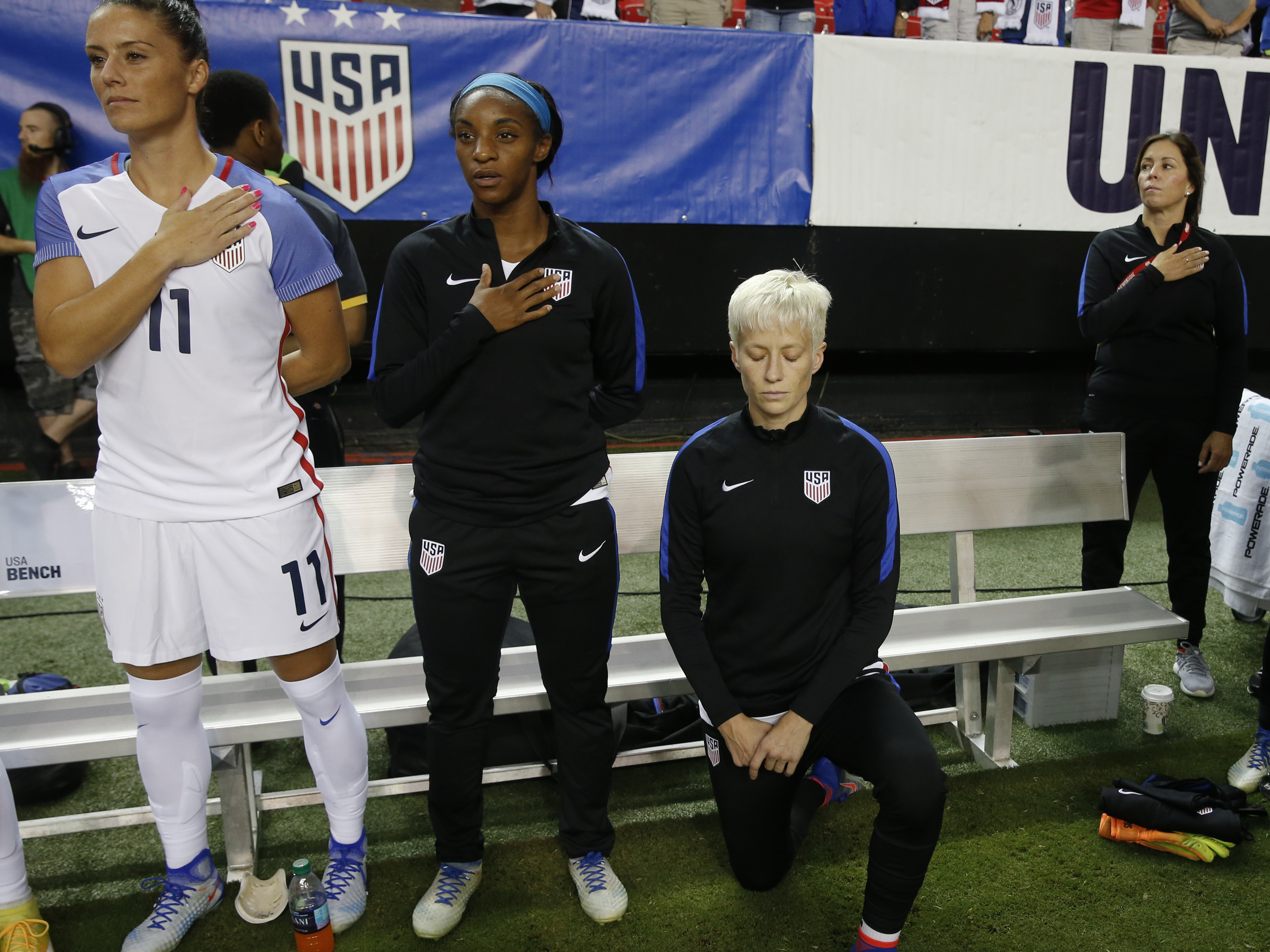 caption: USA's Megan Rapinoe (right), kneels next to teammates Ali Krieger and Crystal Dunn as the national anthem is played before an exhibition soccer match against Netherlands on Sept. 18, 2016, in Atlanta.