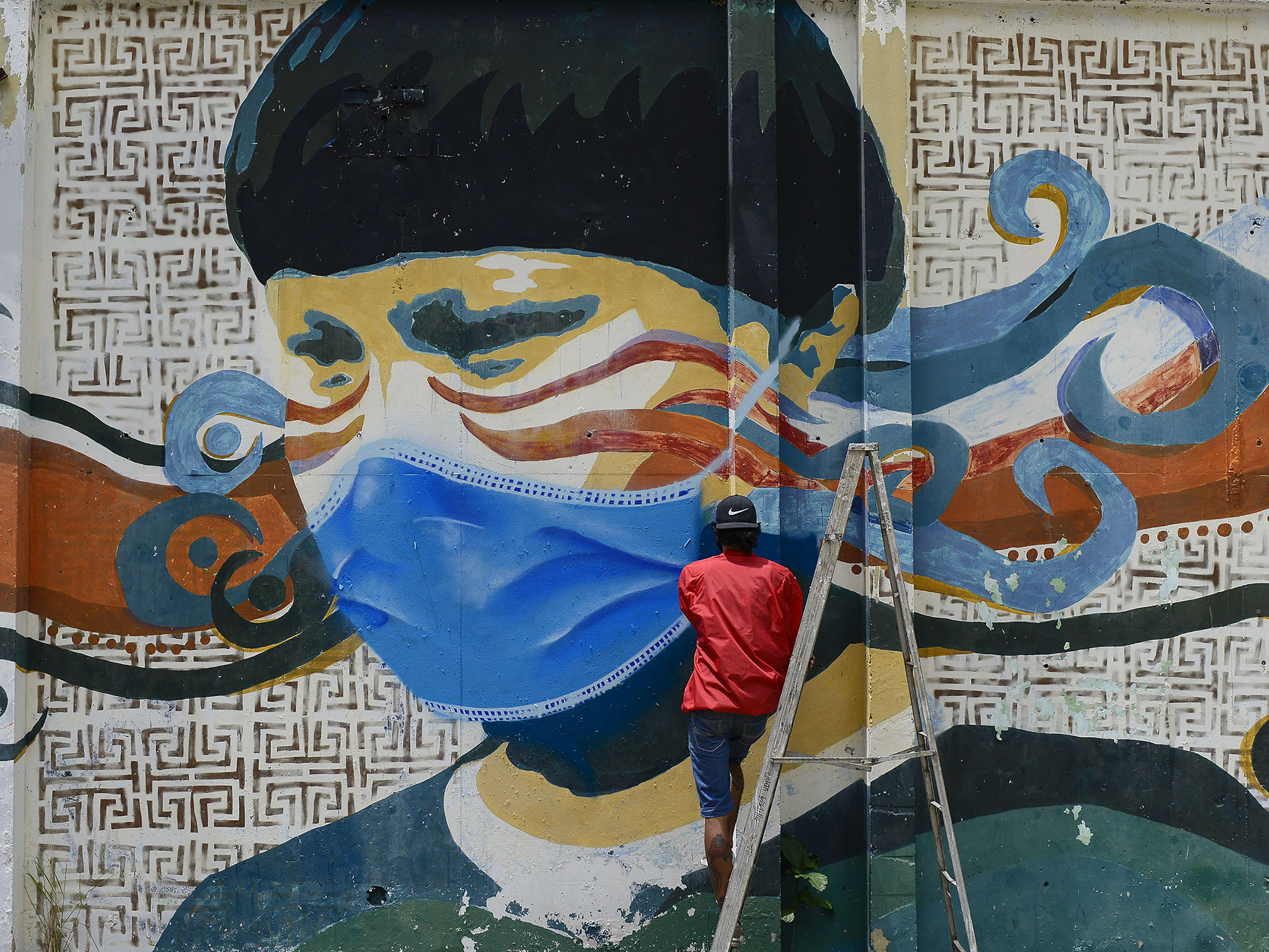 caption: A street artist spray-paints a protective face mask over an old mural featuring a Venezuelan Indigenous man in Caracas, Venezuela, on Saturday. Globally, new daily cases hit an all-time high on Saturday, the World Health Organization reports.