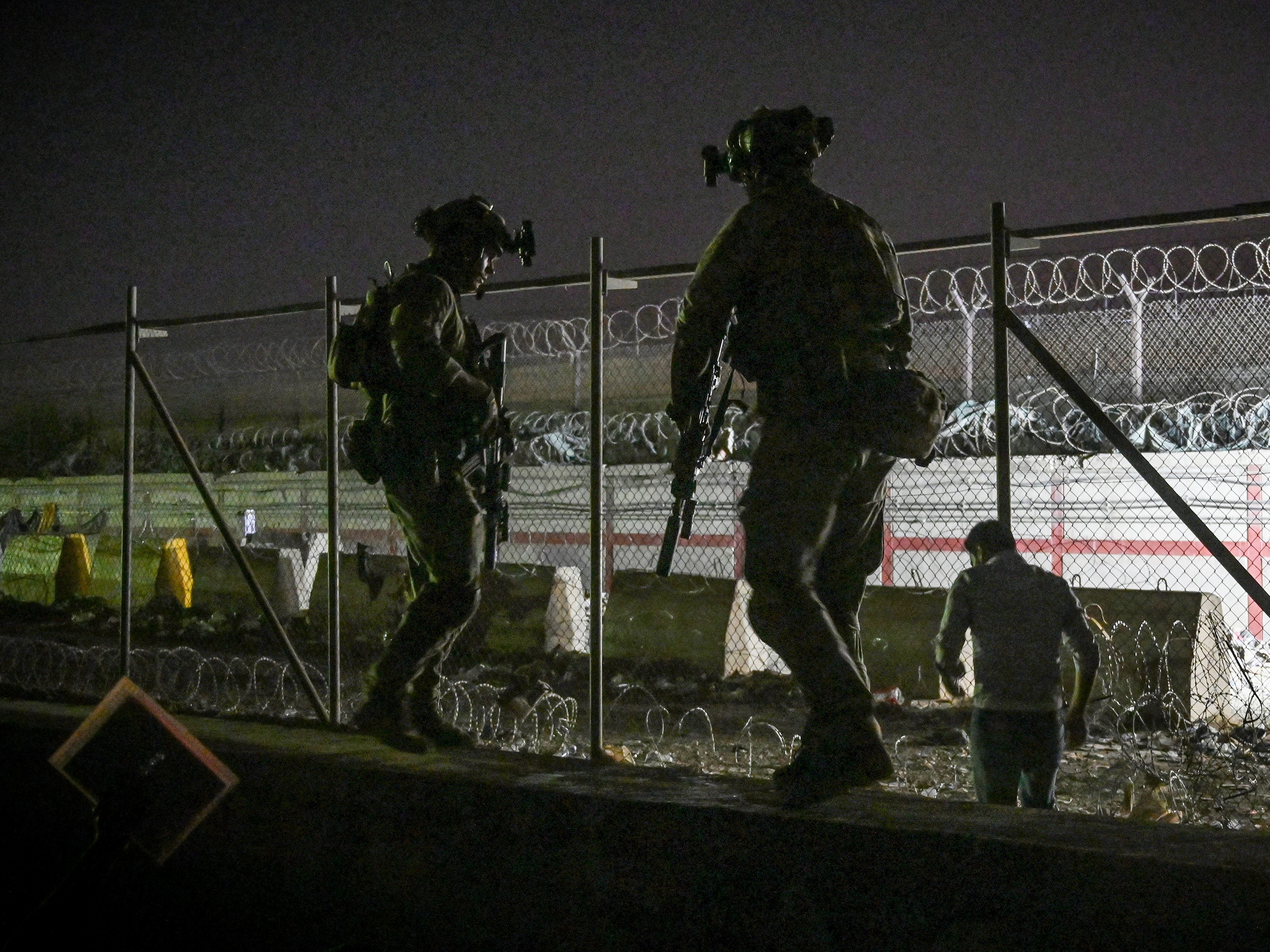 caption: British and Canadian soldiers stand guard late Sunday near a canal as Afghans wait outside the foreign military-controlled part of the airport in Kabul, hoping to flee the country following the Taliban's military takeover of Afghanistan.