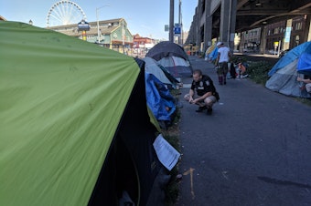 caption: Tents are lined up under the viaduct in Seattle as members of the City's Navigation Team are doing outreach. 
