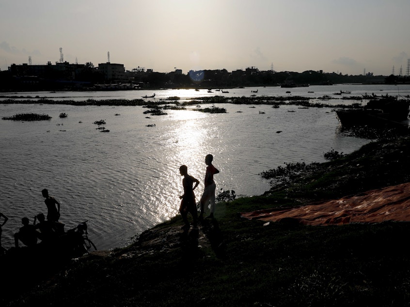 caption: Two boys stand at the edge of the Buriganga River in Dhaka, Bangladesh, in July. A recent study finds that globally, boys and young men made up two-thirds of all deaths among young people in 2019.