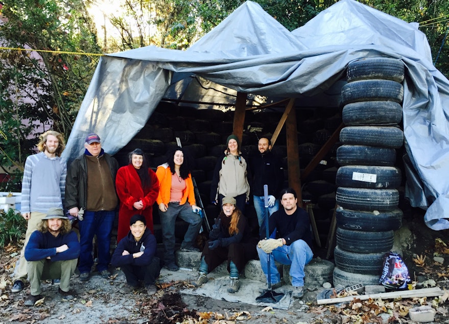 caption: Roxanne Fonder Reeve (red jacket) stands with volunteers from Earthship Seattle in front of their trash studio in progress.