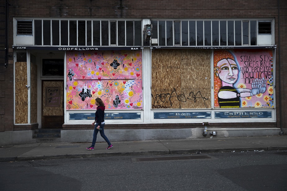 caption: Leslie Buker walks by Oddfellows Cafe + Bar, with a mural painted by Stacy Milrany displayed, on Sunday, March 22, 2020, on 10th Avenue in Seattle.