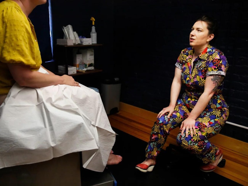 caption: Dr. Stephanie Arnold, who prefers bright-colored clothes instead of a white coat, meets with a patient who needs a pelvic exam. The family medicine clinic Arnold founded offers reproductive health care, including abortion, alongside all kinds of other care. “It’s a little bit of everything, which is very typical of family medicine,” she says.