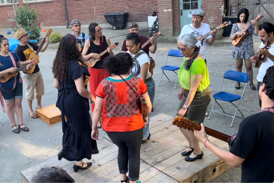 caption: Members of Seattle Fandango Project at an outdoor gathering in the back of the Seattle Amistad School. Several members are dancing on the tarima.