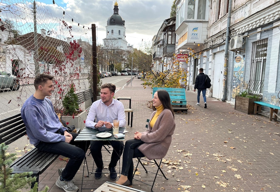 caption: From left: Ivan Sushchyk, Vadym Zahozytsky and Yana Yelizarova discuss U.S. support for the war in Ukraine at a coffee shop in Kyiv on Oct. 11.
