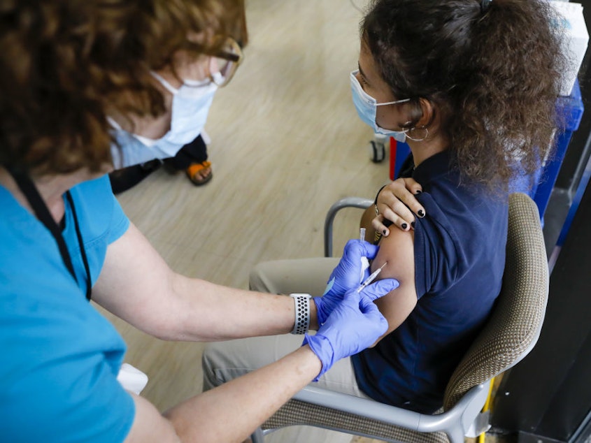 caption: The CDC has softened its guidance for how to operate summer camps for kids this year. Children 12 and older can get the COVID-19 vaccine. Here, a health care worker administers a vaccine dose to a teenager in Miami.