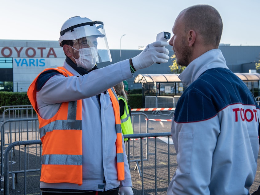 caption: A worker wearing protective gear checks an automobile assembly line worker's temperature at the entrance to a Toyota plant in Onnaing, France, on April 21. U.S. auto plants are preparing to reopen with new coronavirus safety protocols.